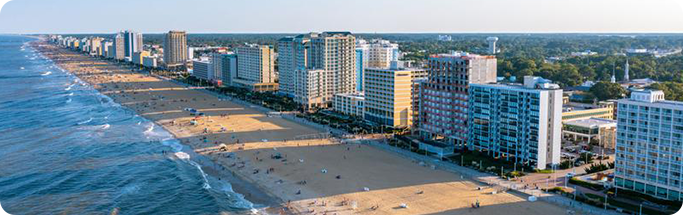 Aerial view of Virginia Beach with ocean waves, sandy shore, and high-rise hotels lining the bustling boardwalk.