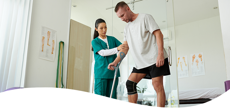 Physical therapist assisting a man with a knee brace during rehabilitation exercises in a clinic.